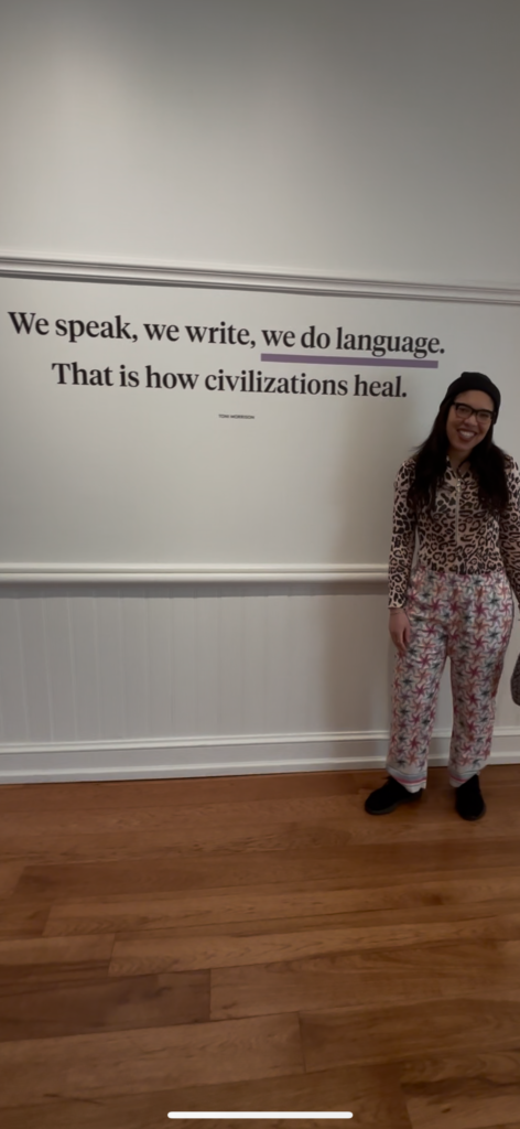 a woman stands in front of a Toni Morrison quote