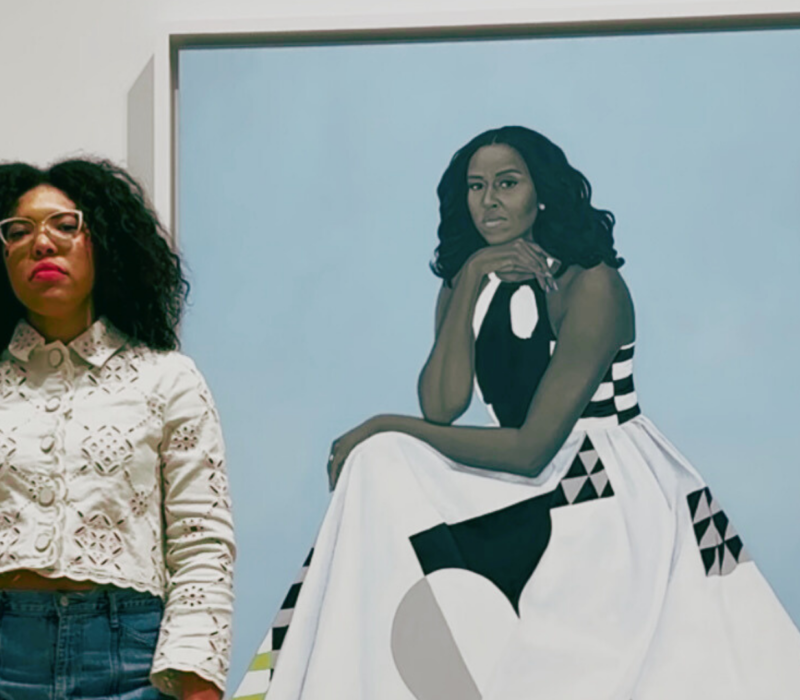 woman stands next to painting of First Lady Michelle Obama