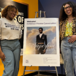 two women stand on either side of a poster advertising a new show at the Met