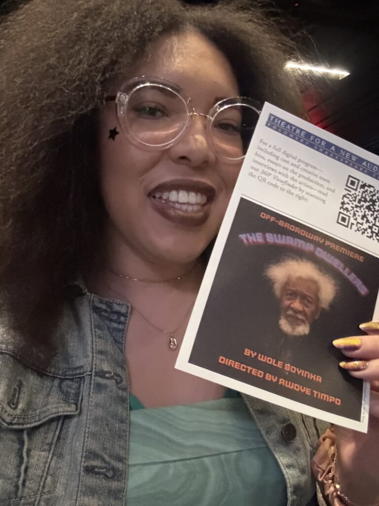 a woman with a black star holds up a theatre program in a selfie