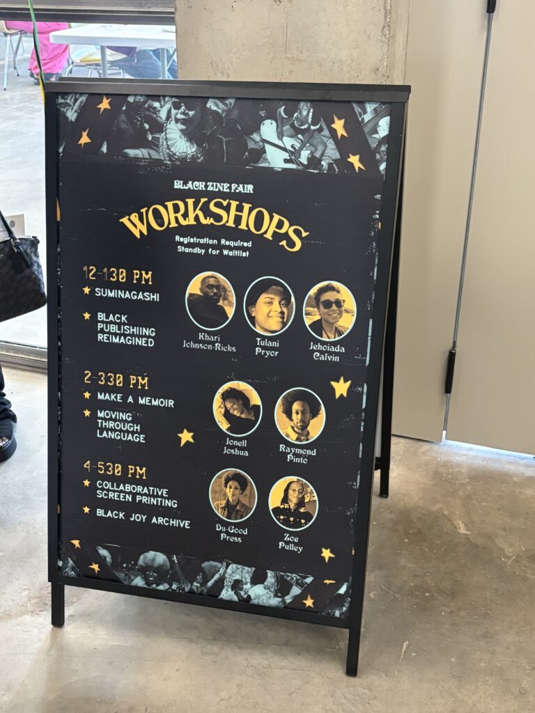 A standing floor sign holds a poster with a list of workshops. It features facilitator names and photos along with workshop titles and times.
