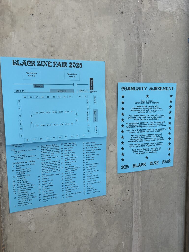 Blue papers are taped on a concrete wall. The papers show a diagram of the fair, a list of participating vendors, and a list of community agreements.