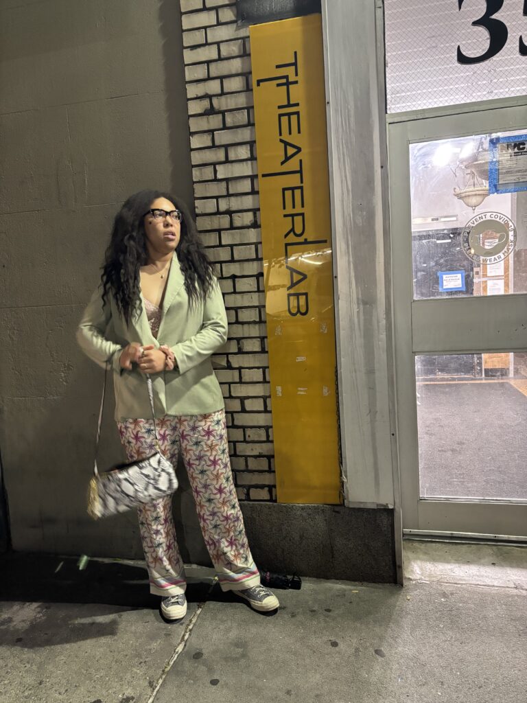 a woman stands next to a small vertical sign that reads TheaterLab