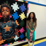 Woman stands next to a colorful quilt that features a regal Black boy.