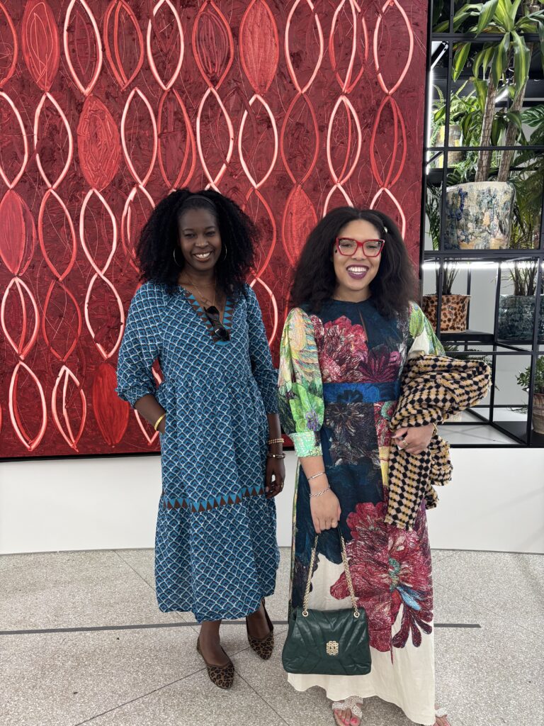 two women smile in front of artwork