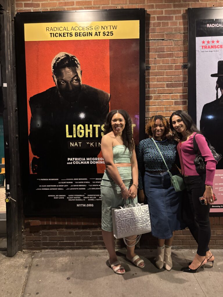 Three women pose in front of a poster
