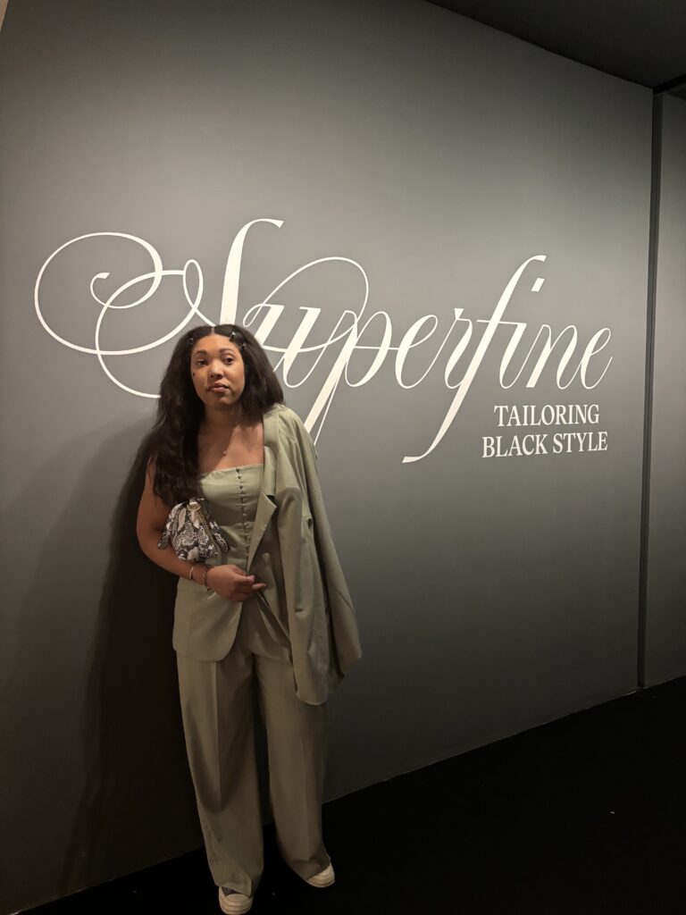 a woman stands in front of a wall that reads Superfine