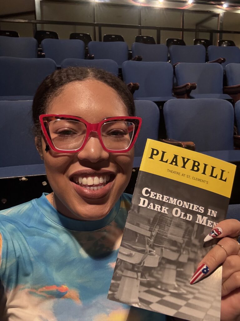 a woman smiles with a playbill for the show "ceremonies in dark old men"
