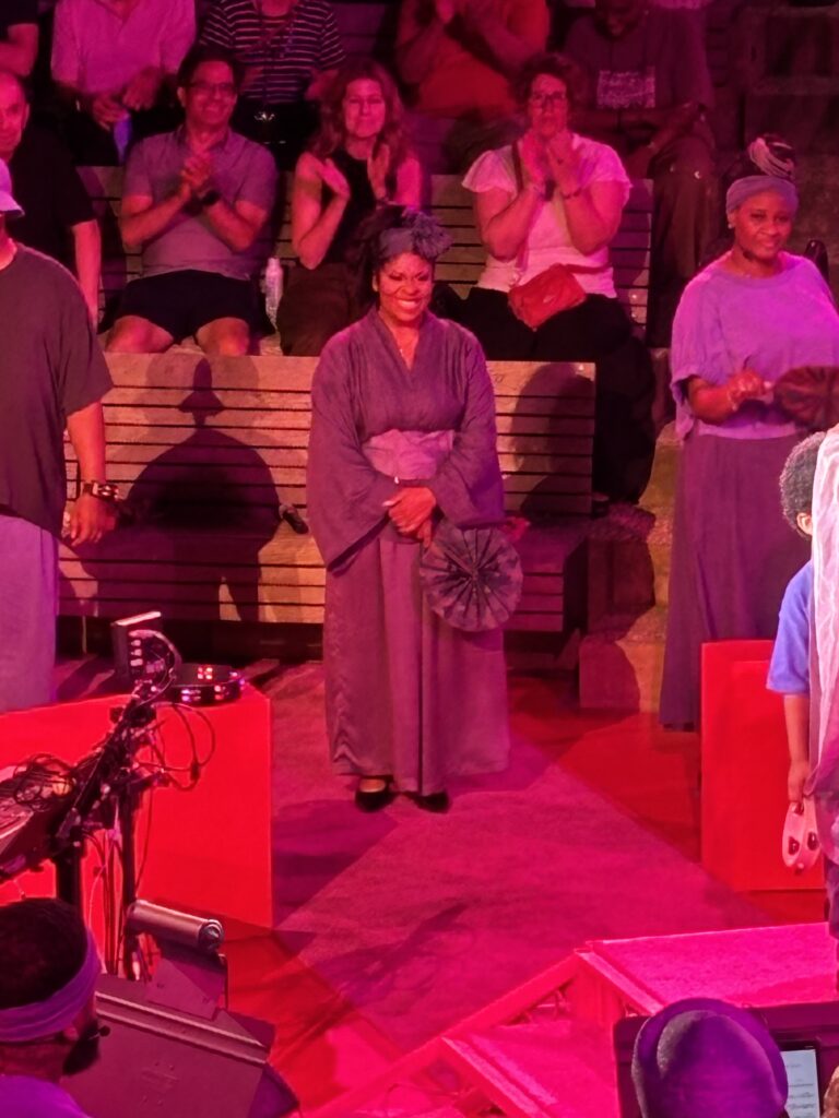 Kim Burrell stands on a red stage in a purple ensemble