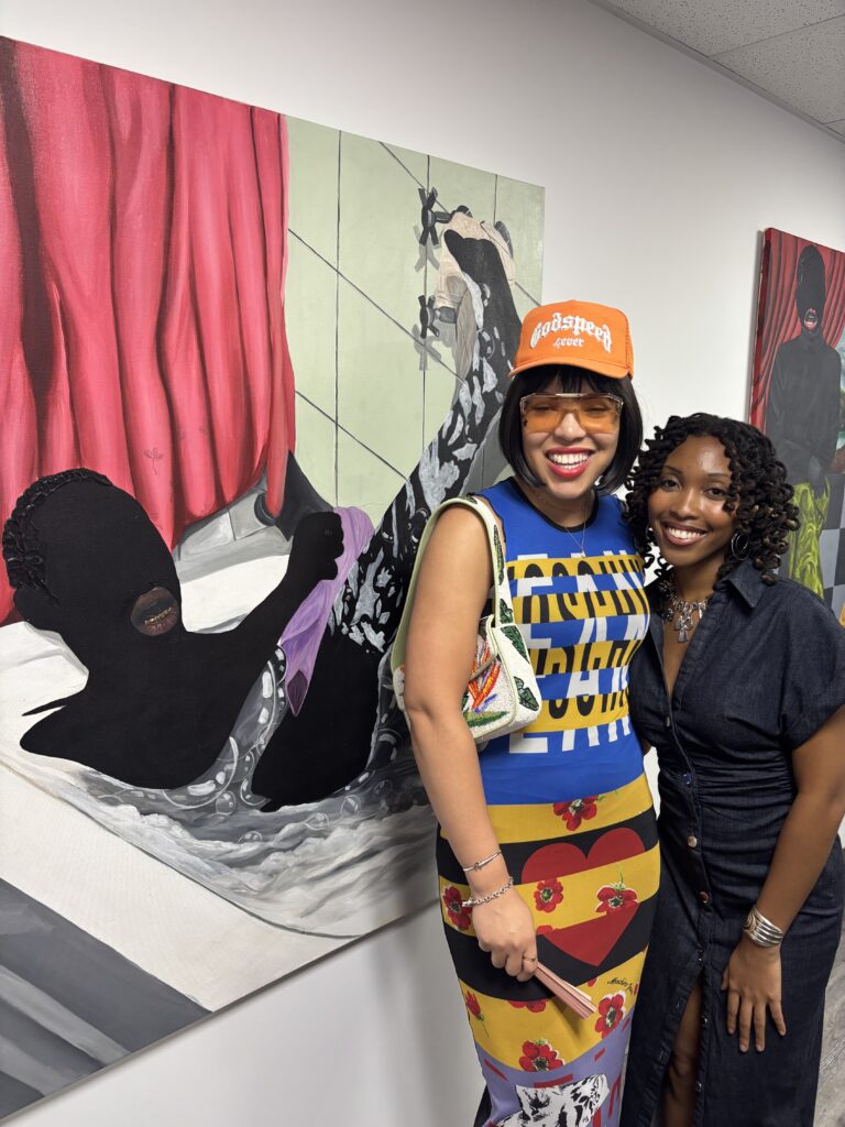 two women standing in front of artwork smiling