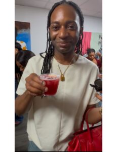 a man with long dreadlocks holds a red drink and a red handbag