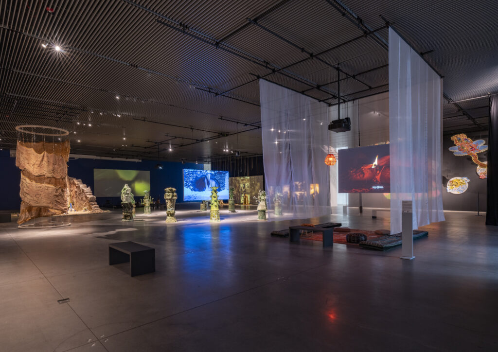 view of a large, dimly lit room with various artworks like video, sculpture, and paintings