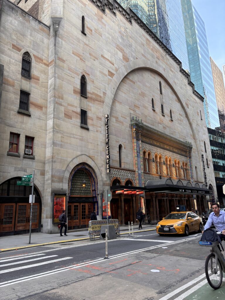 Exterior view of City Center shown from across the street. There is a yellow cab passing in front of the building. 