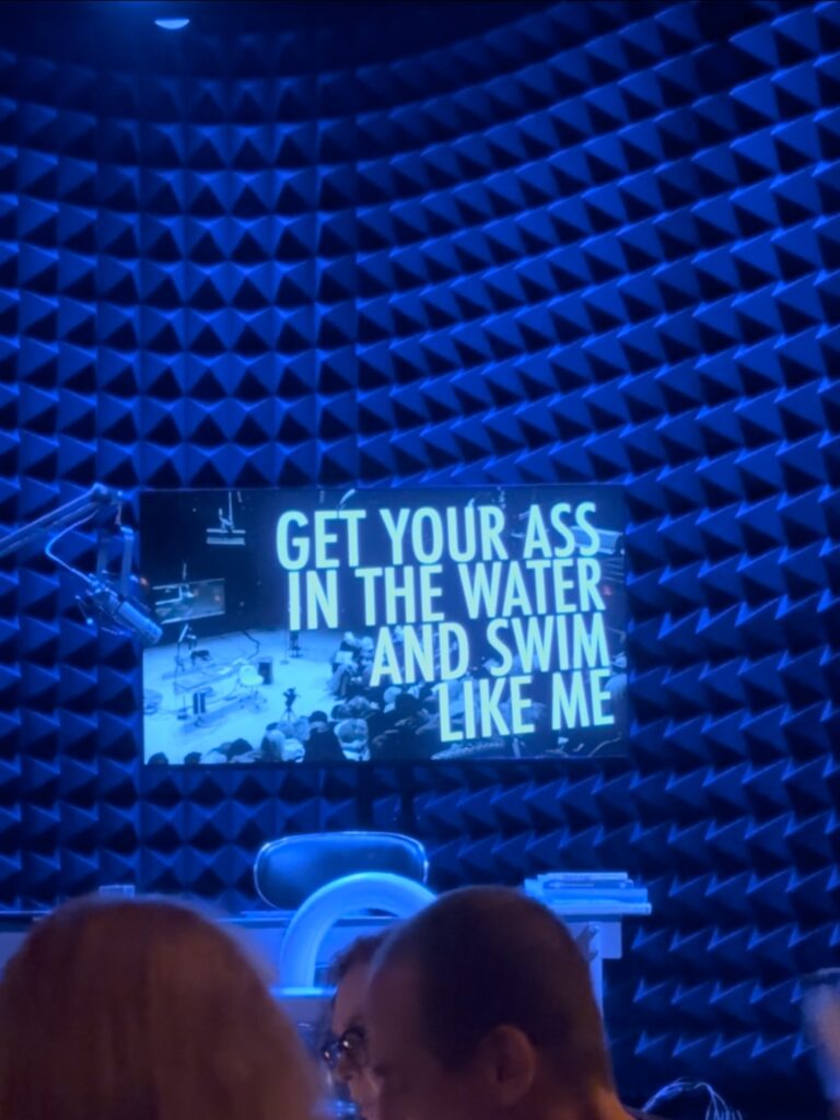 A padded wall with a TV in the forefront that displays the title of the show