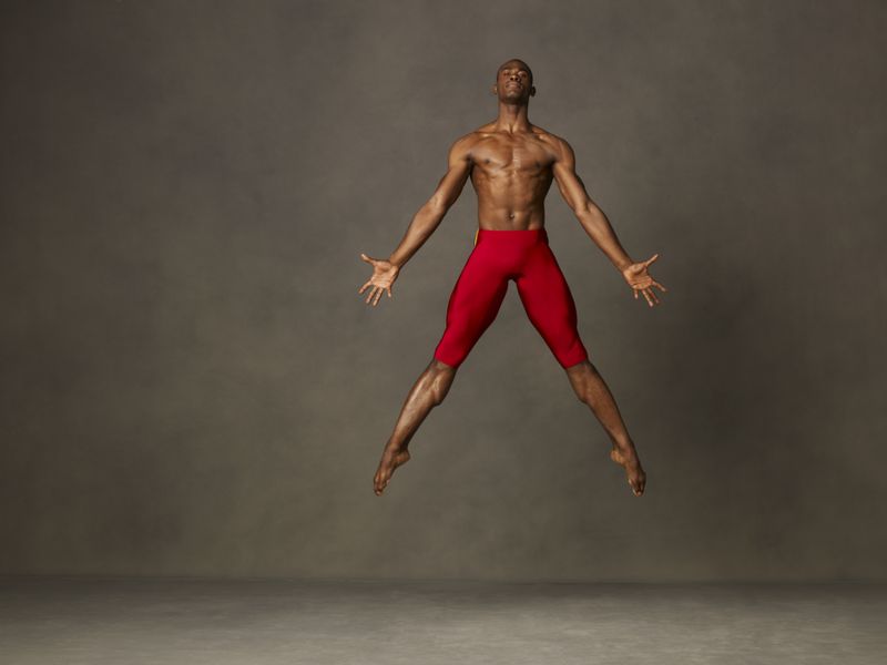 A man wearing tight red shorts is suspended mid-jump with his body in a perfect jumping jack