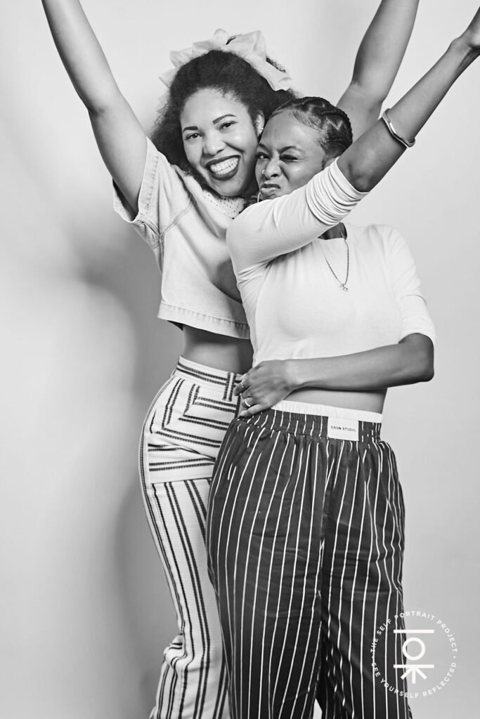 Two women in striped pants hold their hands up and make fun faces (black and white photo)