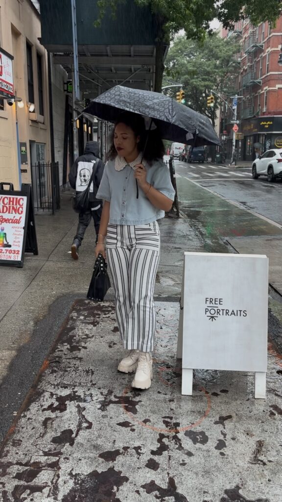 A woman with an umbrella stands next to a sidewalk tent that says "Free Portraits"